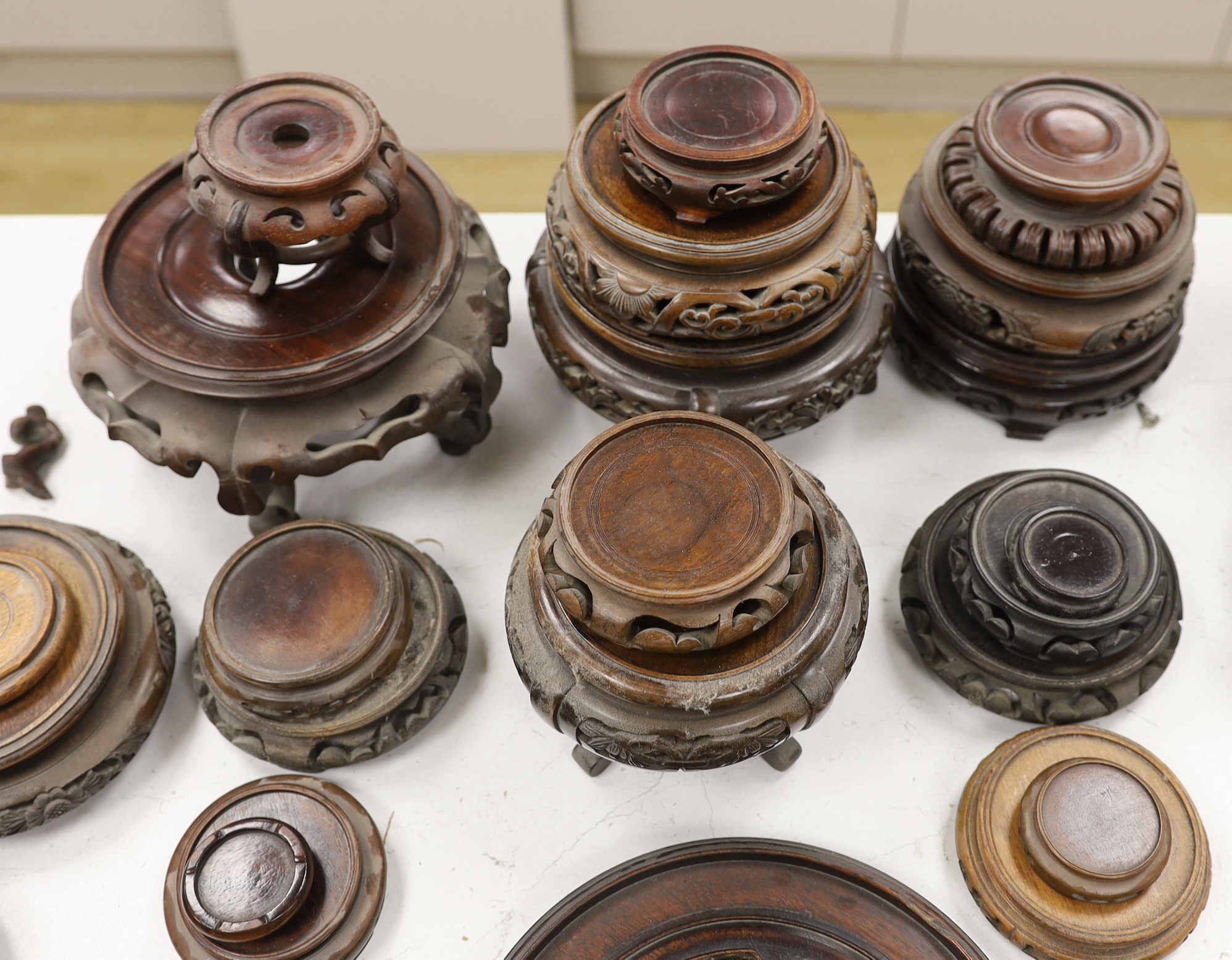 Twenty five assorted Chinese hardwood vase stands and two carved wooden vase covers, largest stand 22cm diameter